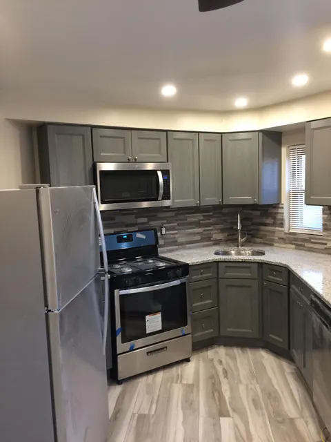 Remodeled kitchen with gray cabinets, granite countertops, stacked stone backsplash, and stainless appliances