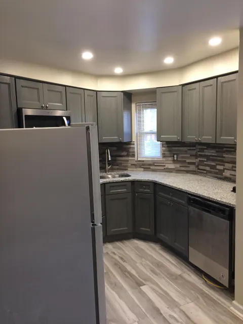 Gray shaker kitchen cabinets with granite counters, stone backsplash, and wood-look tile floor