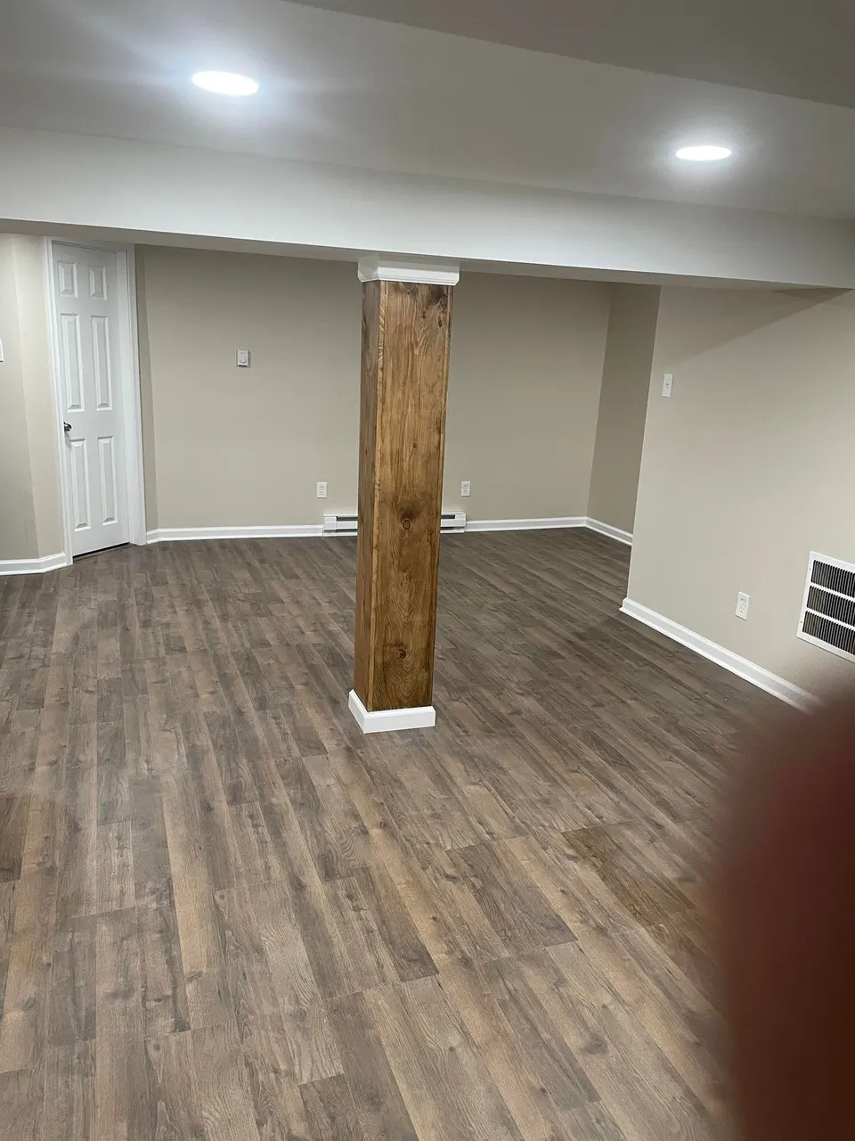 Finished basement family room with luxury vinyl plank flooring and stained wood support column