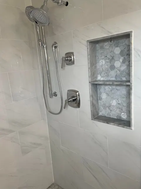 Marble-look tile shower with chrome rain head, handheld sprayer, and hexagon mosaic niche