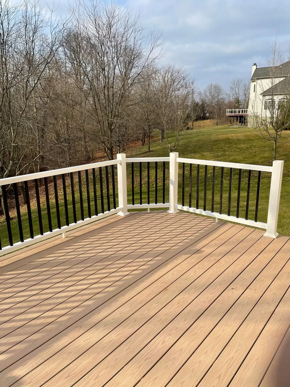 Composite deck with white railing and black balusters overlooking a spacious backyard