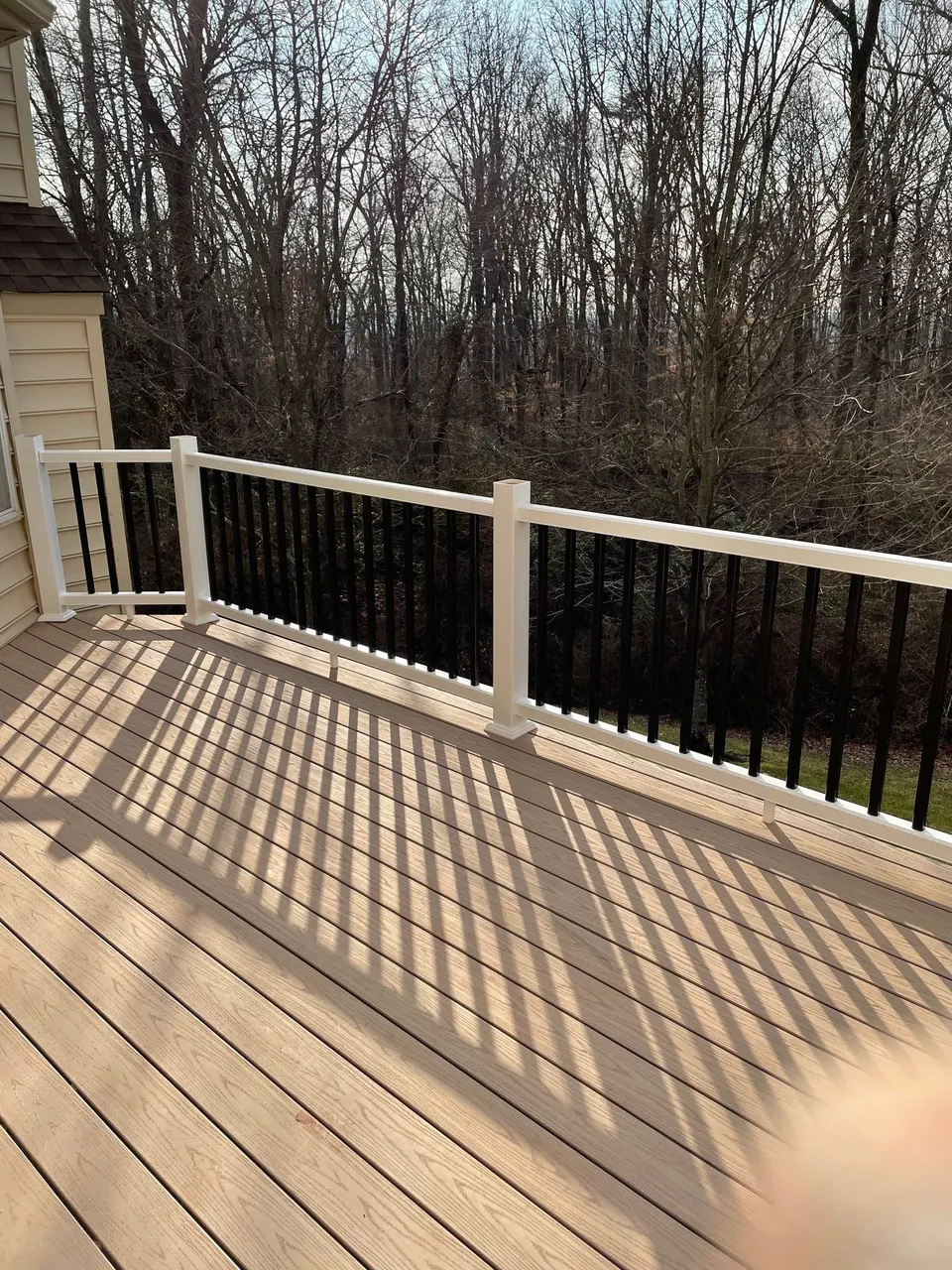 Sunlit composite deck boards with new white vinyl railing and black aluminum balusters