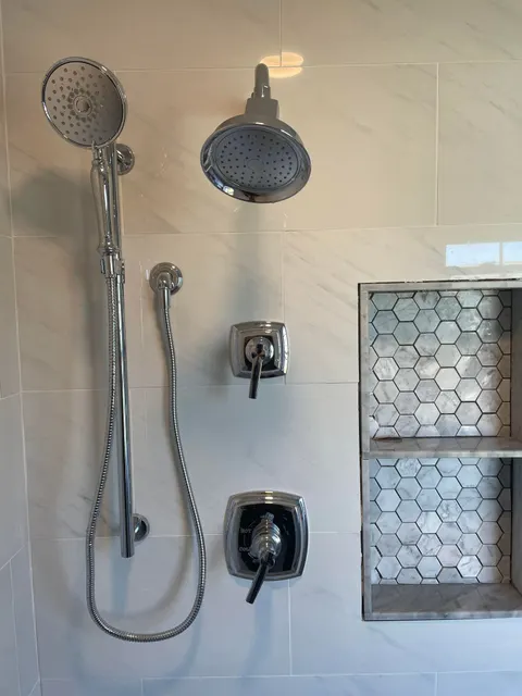 Polished chrome shower fixtures with marble hexagon tiled storage niches in tiled shower