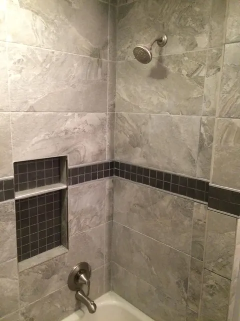 Completed tub shower with gray tile walls, mosaic accent band, and recessed niche
