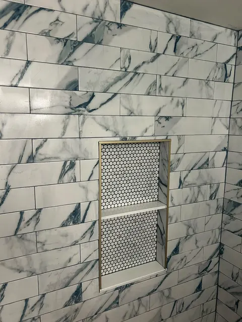 Recessed shower niche with white penny tile back, center shelf and brushed gold edge trim in marble-look subway tile