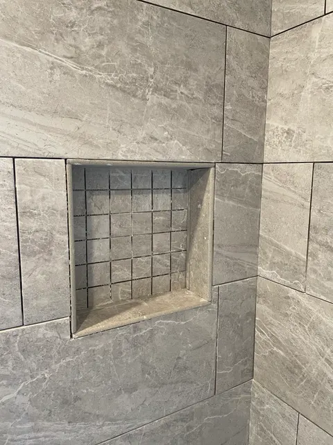 Recessed shower niche with mosaic tile backing set into gray stone-look wall tile