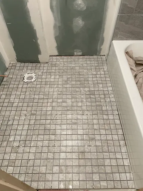 Gray mosaic shower pan tile installation beside soaking tub during bathroom remodel