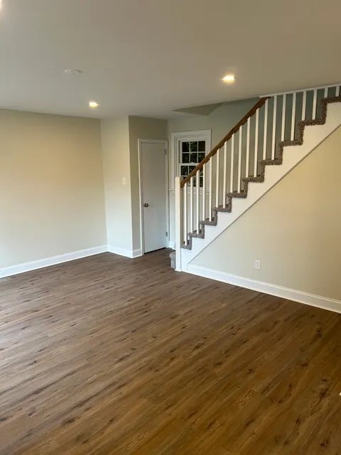 Bright open living space with new wide-plank flooring and carpeted staircase with wood handrail