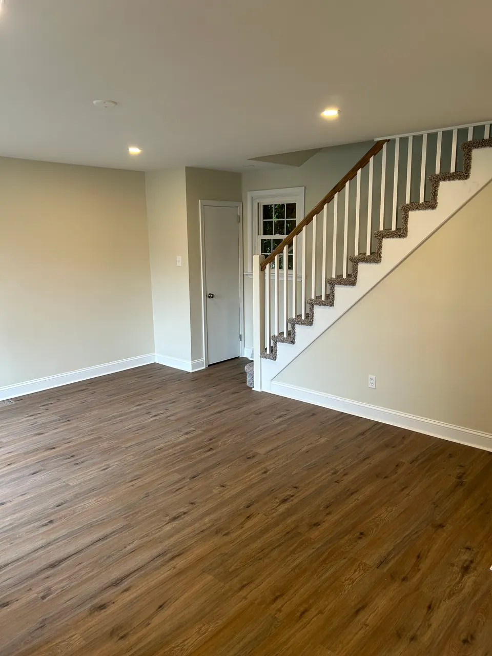 Bright open living space with new wide-plank flooring and carpeted staircase