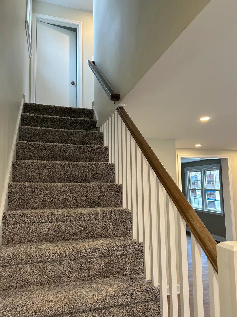 Newly carpeted staircase with white risers, painted spindles, and stained oak handrail
