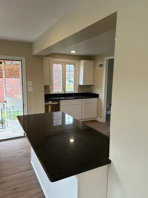 Remodeled kitchen with polished black granite peninsula and white shaker cabinetry