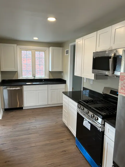 New gas range and vent hood installed in kitchen with granite counters and white cabinets