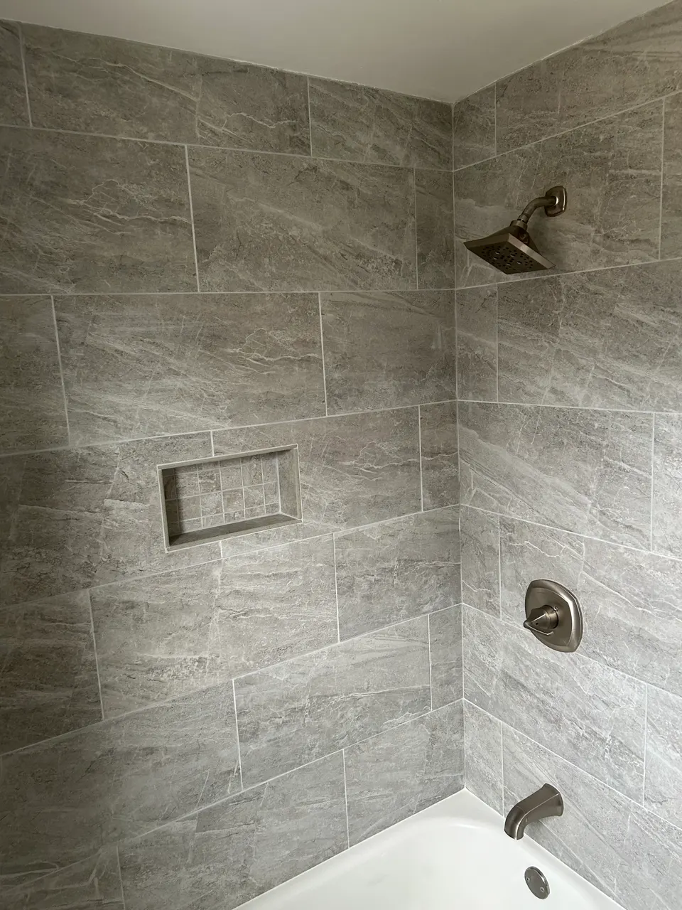 Completed tub shower surround in gray stone-look tile with brushed nickel fixtures