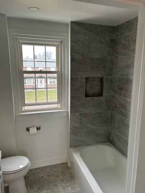 Renovated bathroom with floor-to-ceiling tiled tub surround, recessed niche, and new toilet