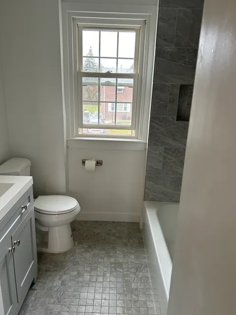 Remodeled bathroom with gray stone tile shower, mosaic accent wall, and white vanity