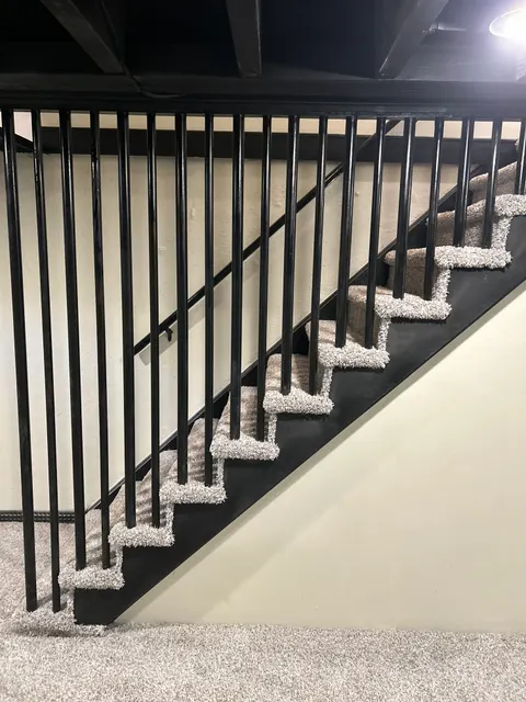 Finished basement staircase with new gray carpet and black metal railing