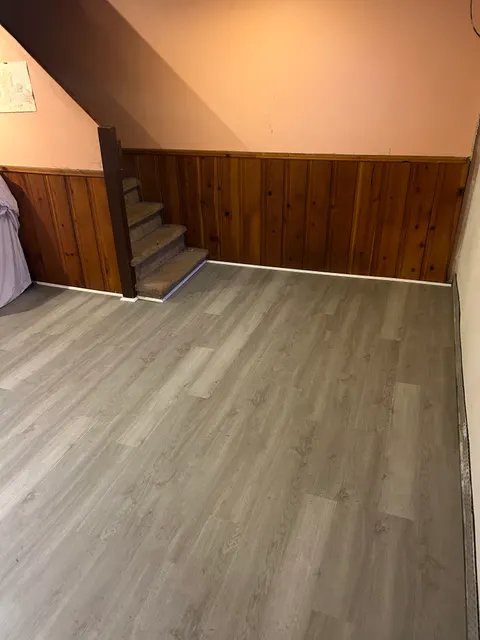 Gray luxury vinyl plank flooring meeting staircase in pine paneled room
