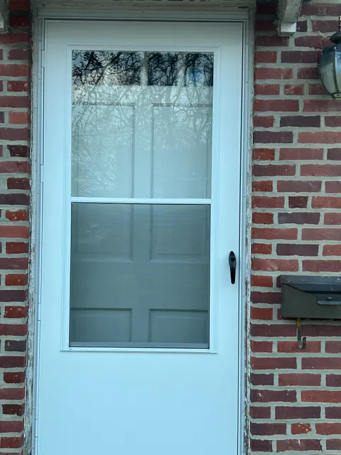 New white aluminum storm door with screen installed on brick home