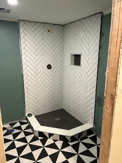 Custom shower with white herringbone tile walls, niche, and black penny tile pan