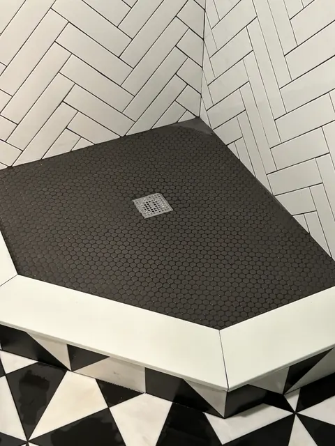 Black penny tile shower pan with white curb and herringbone tile walls