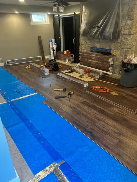 Wide-plank luxury vinyl flooring installation in progress in living room with stone fireplace
