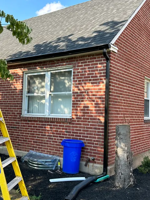 New black aluminum gutter and downspout installed on brick home exterior