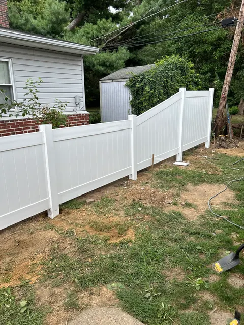 New white vinyl privacy fence panels installed along regraded backyard