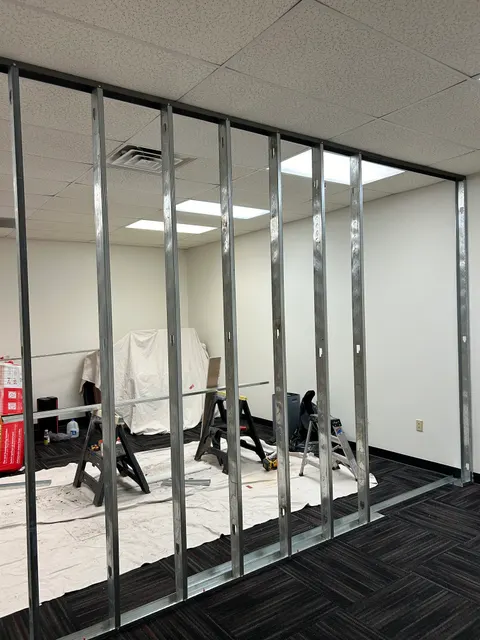 Metal stud wall framing in progress for office buildout beneath drop ceiling