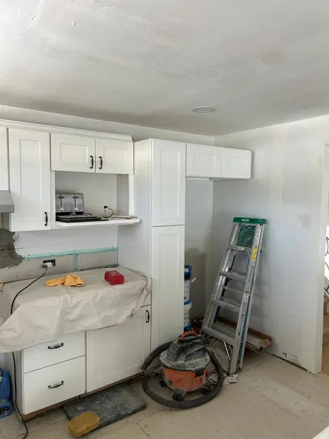 White shaker cabinet installation underway in kitchen remodel with fresh drywall