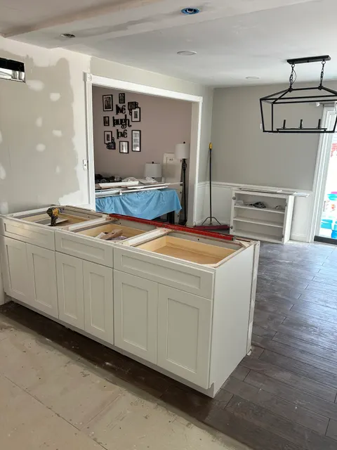 Kitchen remodel in progress with new white shaker pantry cabinets and wood-look tile floor