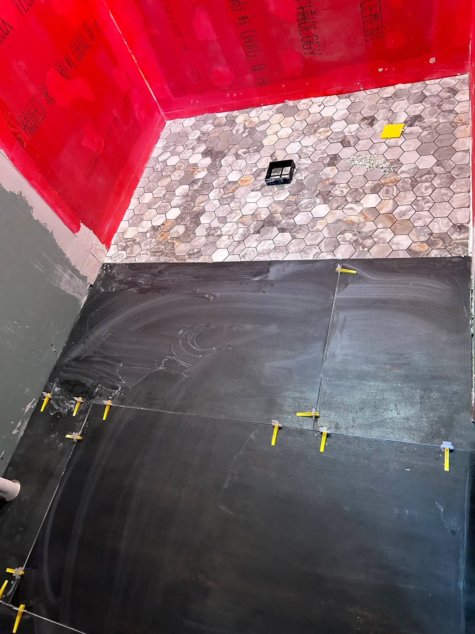 Shower renovation in progress with red waterproofing membrane and dark large-format tile