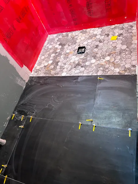 Shower renovation in progress with red waterproofing membrane and dark large-format tile