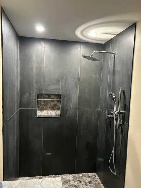Completed walk-in shower with charcoal tile, rain shower head, and marble mosaic accent
