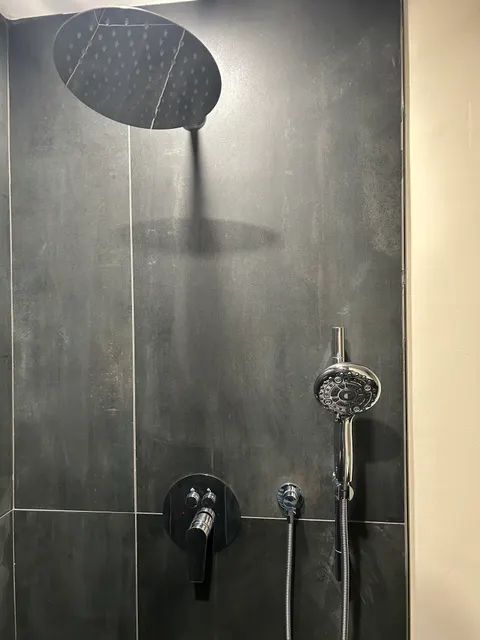 Chrome rain head and handheld shower fixtures on charcoal large-format tile wall