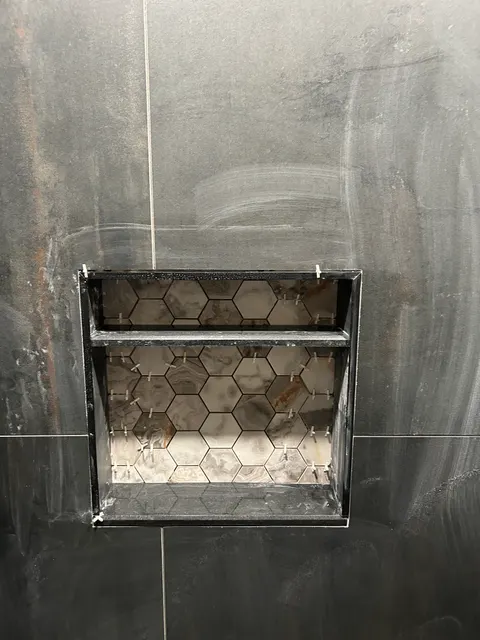 Recessed shower niche with marble hexagon mosaic set in dark slate-look wall tile
