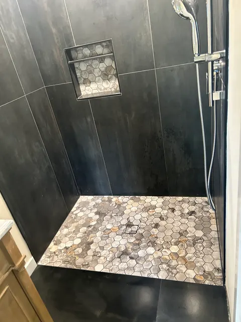 Custom shower with dark metallic tile, hexagon stone accent wall, and mosaic niche
