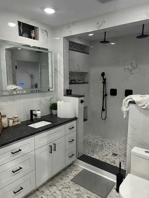 Remodeled bathroom with marble-look tile, matte black fixtures, white vanity, and LED mirror