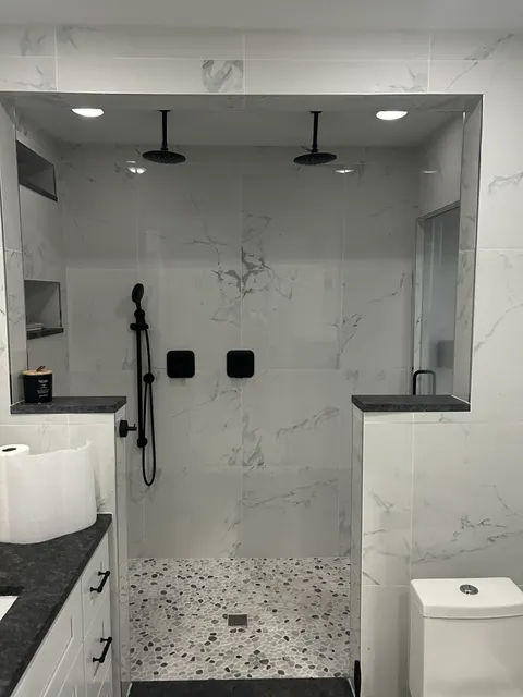 Walk-in marble tile shower with dual black rain heads and pebble stone floor