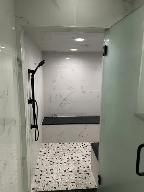Marble tile shower interior with matte black handheld fixture and pebble accent floor