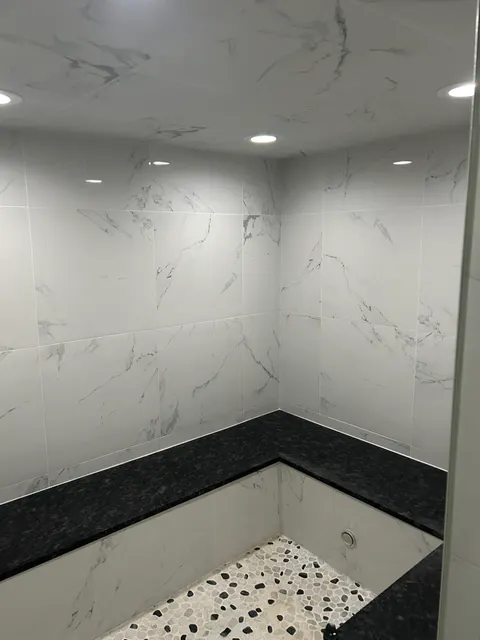 Marble-look tile shower with built-in bench and gray pebble mosaic floor