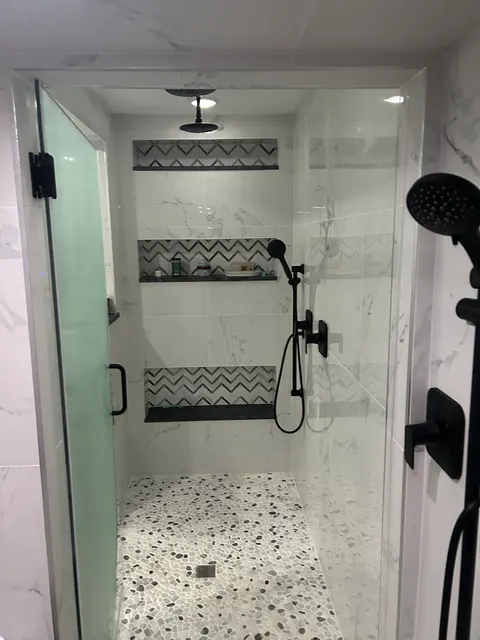 Glass-enclosed marble shower with dual rain heads and chevron mosaic storage niches