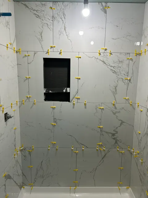 Large-format marble-look shower wall tile being set with leveling clips