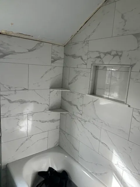 Tiled tub surround with storage niche and corner shelves nearing completion
