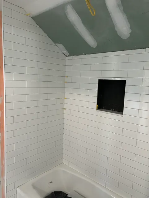 White subway tile tub surround in a running-bond pattern with a recessed niche, mid-installation