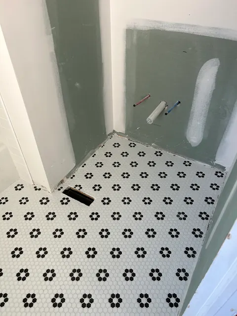 Black flower-pattern hexagon mosaic tile floor installed in bathroom remodel