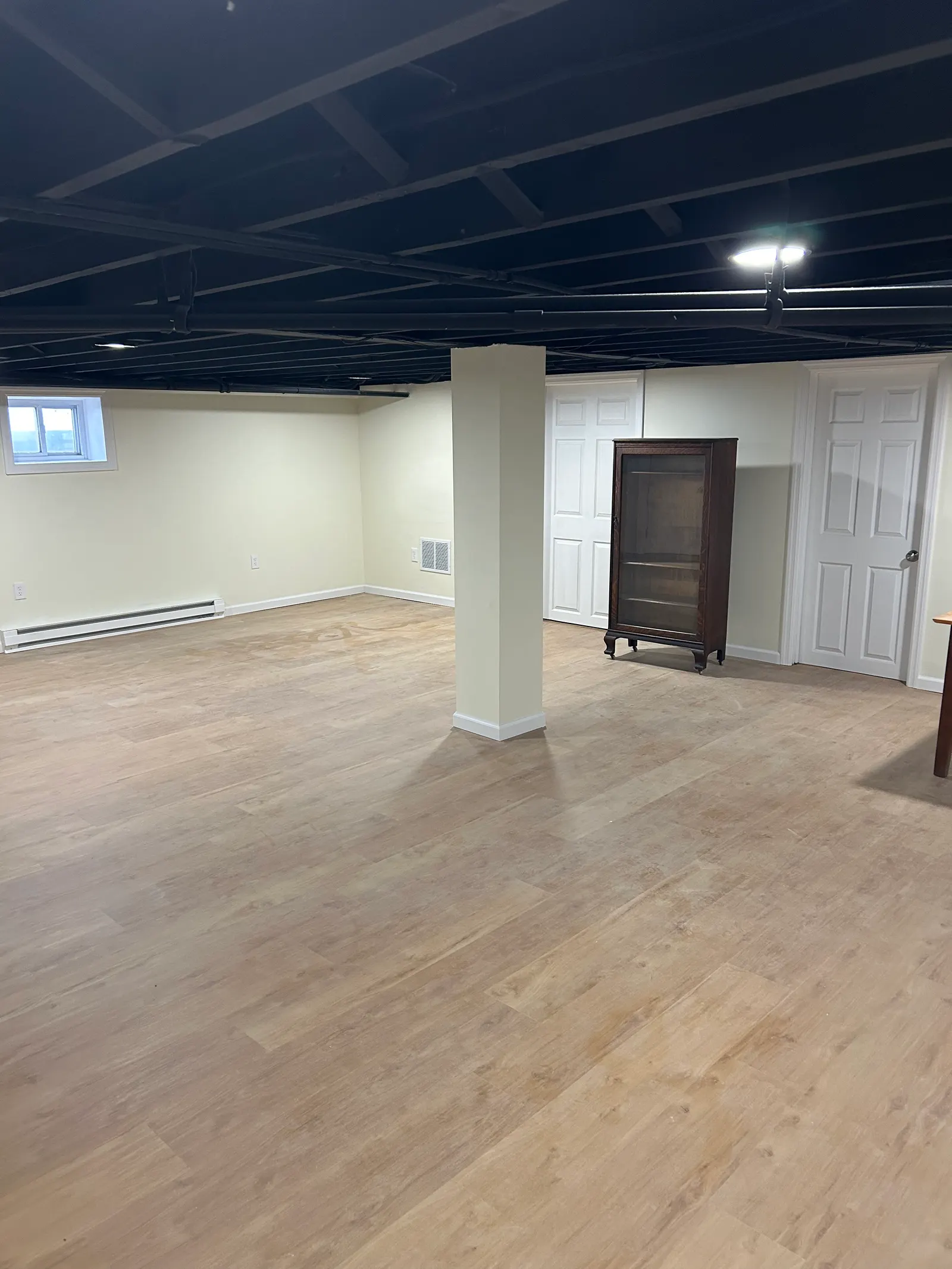 Finished basement living area with wood-look vinyl plank flooring and industrial black ceiling