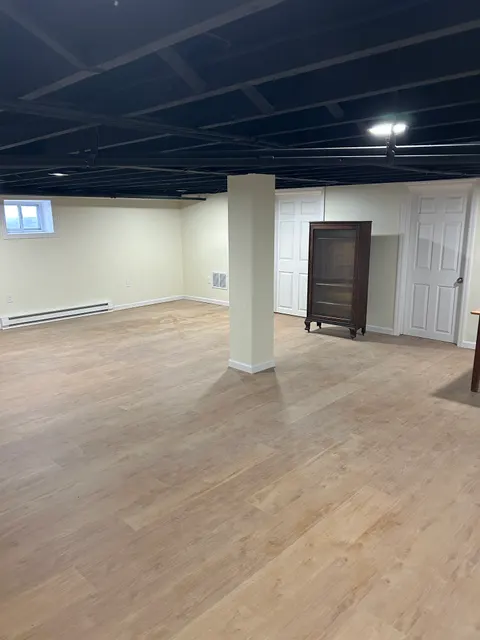 Finished basement living area with wood-look vinyl plank flooring and industrial black ceiling