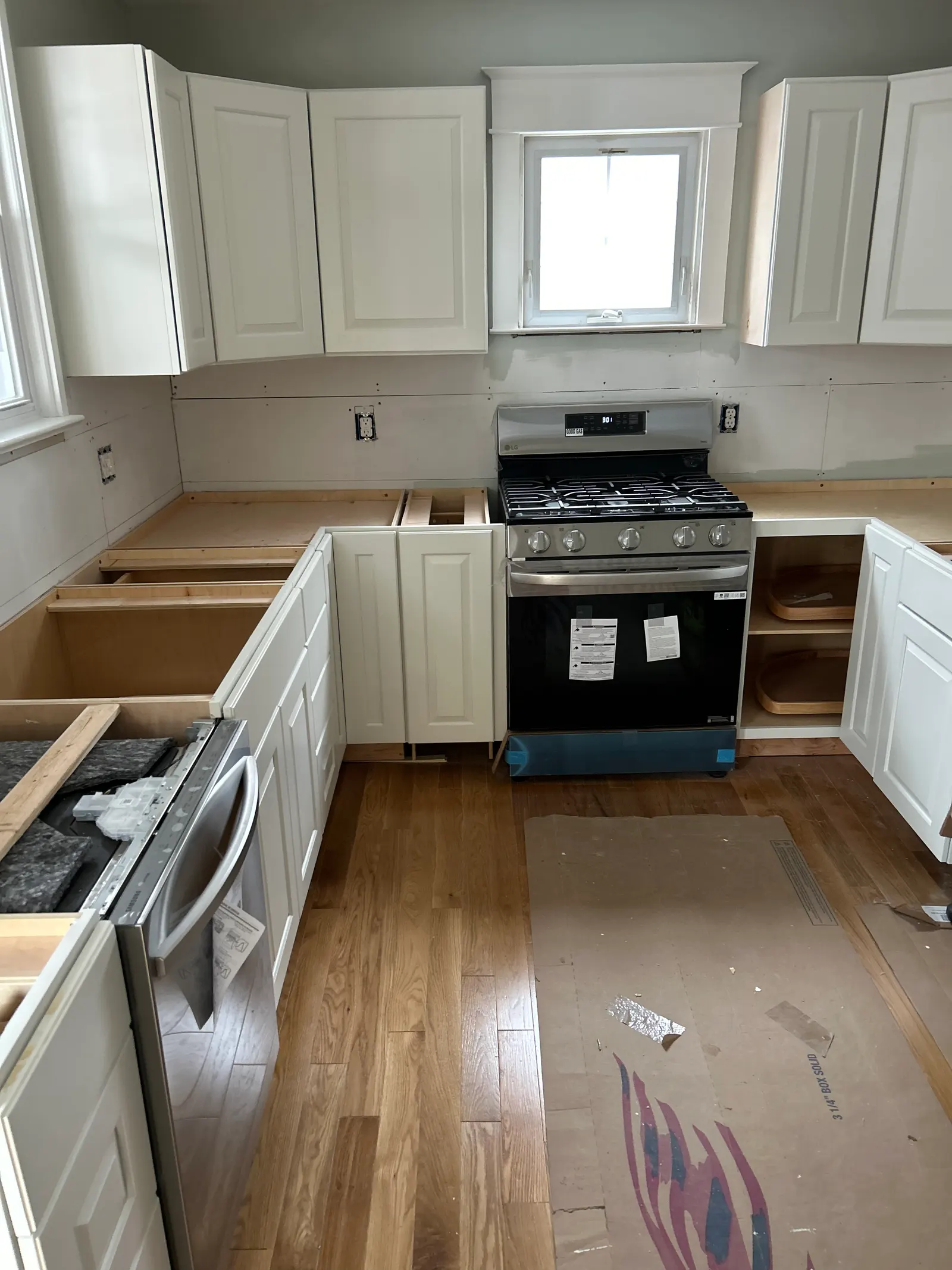 Kitchen remodel in progress with new white cabinets, gas range, and protected hardwood flooring