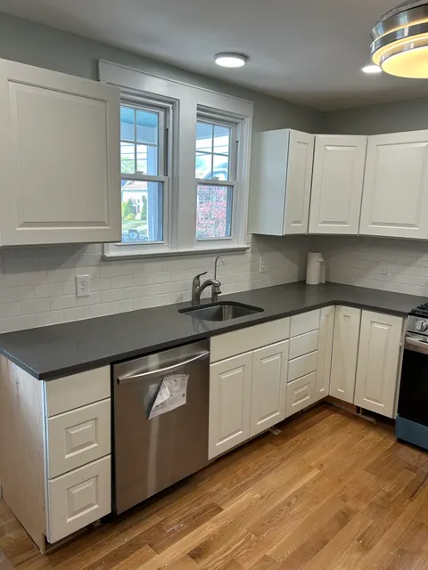 Completed kitchen with white raised-panel cabinets, quartz countertops, subway tile, and oak floors