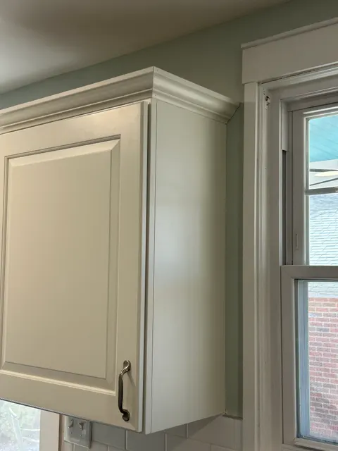 Cabinet crown molding detail with brushed nickel hardware beside kitchen window